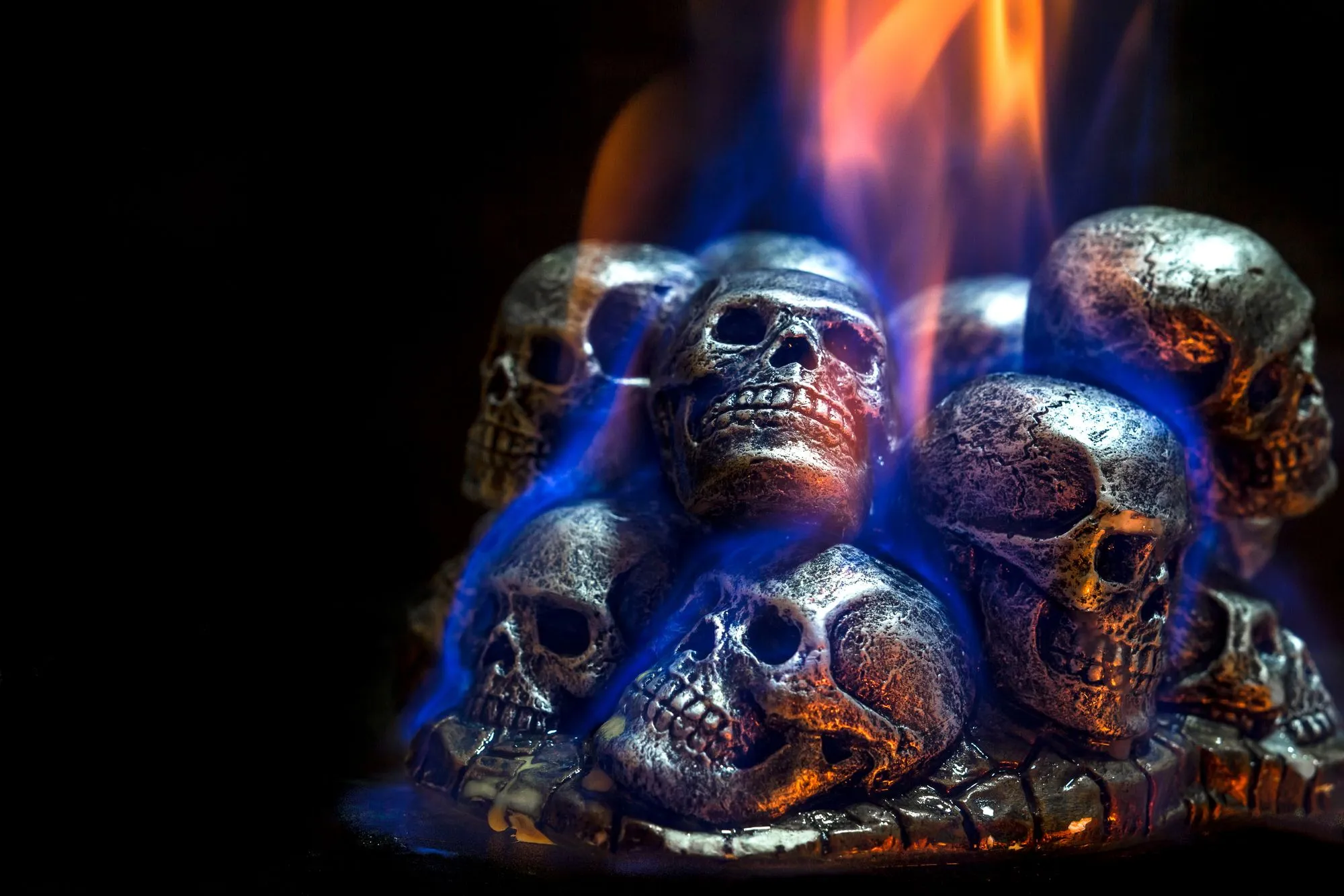 A mound of ceramic skulls stacked in a gas fire pit, with blue and orange flames rising between them.